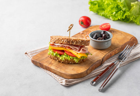 Club sandwich on a plate of bacon, cheese, tomato and lettuce on a wooden board with olives. The concept of a healthy snack for breakfast or lunch. Copy space.の写真素材