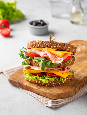 Club sandwich on a plate of bacon, cheese, tomato and lettuce close up on a wooden board with olives. The concept of a healthy snack for breakfast or lunch.の写真素材
