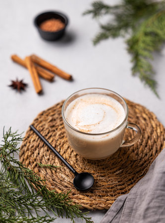 Spiced coffee latte or cappuccino with cinnamon sticks on a light background with fir branches. The concept of a Christmas warming drink. Festive winter mood.の写真素材