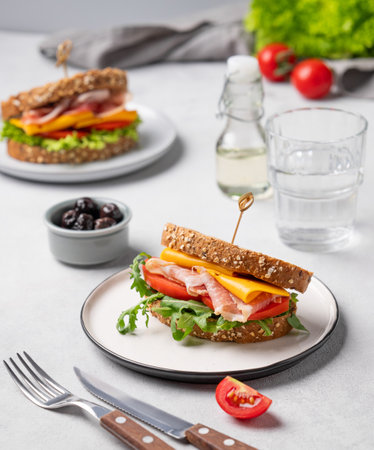 Toast club sandwich made of grain bread with cheddar cheese and bacon stuffed with tomatoes and arugula  on a light background with ingredients. Healthy and dietary breakfast concept.の写真素材