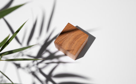 Empty wooden cube with shadows and green leaves on a white background. Layout concept for presentation of promotional products, sale or demonstration of cosmetics. Top view and copy space.の写真素材