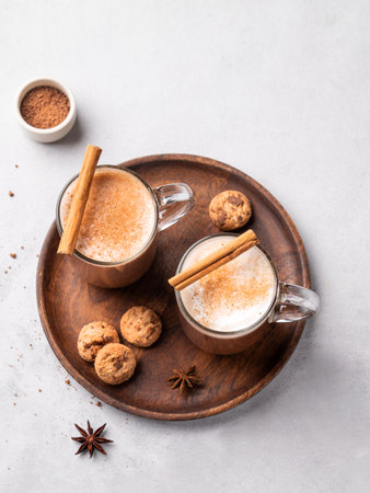 Two glass mugs with hot chocolate and milk foam on a wooden board on a gray background with cinnamon sticks, anise star and cookies. Warming winter drink concept. Top view .の写真素材