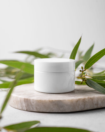 Organic cosmetic cream for body and face skin in a white jar on a marble board with green leaves.  Concept of spa beauty natural product. Front view.の写真素材