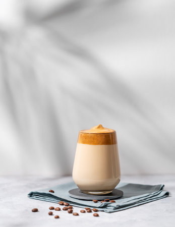 Dalgona coffee. Whipped instant coffee in a glass with beans and shadow on a light background.  The concept of a trendy and popular drink.の写真素材