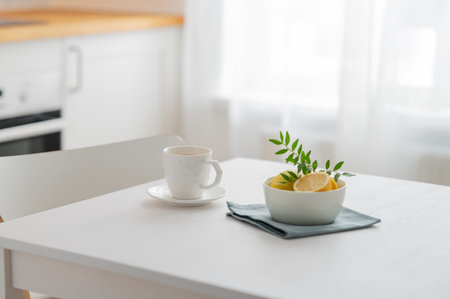 A cup of tea with lemon and a teapot on a white table against the background of a white kitchen with wooden countertop. Interior in modern Scandinavian style. Breakfast concept. Copy space.の写真素材