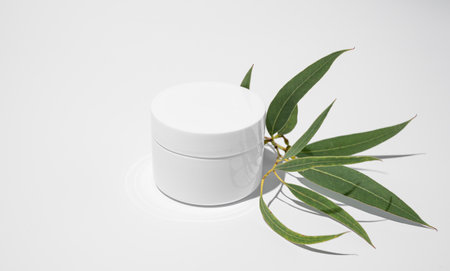 Face and body cream in a white jar on a light background with leaves and hard shadow. Concept of skincare cosmetics with herbs. Health and beauty. Copy space.の写真素材