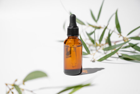 Face and body serum in bottle on a white background with green leaves and shadow. The concept with stage for health and beauty product presentation, sale or cosmetics advertising banner. Copy space.の写真素材