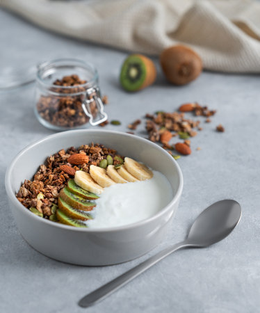 Healthy granola with yogurt, banana and kiwi in a bowl on a light background. Natural homemade dietary breakfast concept made from dairy product, nuts, granola and fresh fruit.の写真素材