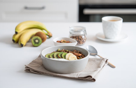 Baked granola with banana and kiwi on the table with cup of tea on a white kitchen background. Healthy breakfast concept of vegetarian yogurt, muesli and fresh fruit.の写真素材