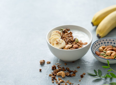 Baked granola with yogurt and banana on a white table. Natural homemade dietary breakfast concept made from dairy product, nuts, muesli and fresh fruit. Copy space.の写真素材