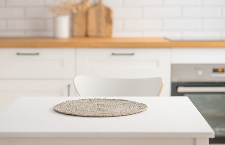 Wooden tabletop with napkin for product montage or mockup against blurred white kitchen with cutting board and brick wall  in scandinavian style in morning light. Copy space.の写真素材