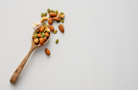 Mix of nuts. Almonds, cashews and pumpkin seeds in a wooden spoon are scattered on a white wooden background. Healthy energy snack concept. Top view and copy space.の写真素材