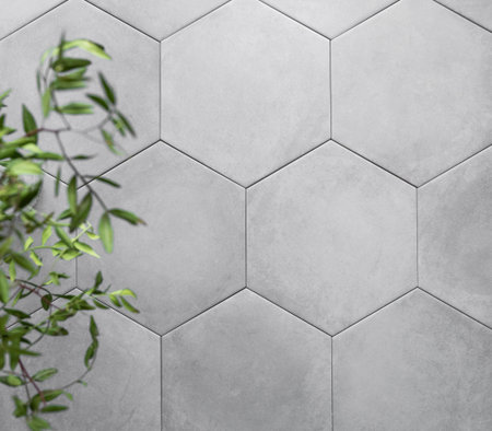 Background of gray hexagon shaped ceramic tiles with green branches. Trendy empty backdrop for...