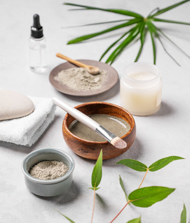 Organic cosmetic with blue clay,  brush, candle and palm leaf on a light background. Concept for preparing homemade skincare cosmetics.の写真素材