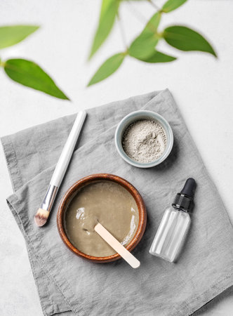 Flat lay of organic cosmetic with blue clay, serum,  brush and branch on a light background. Concept for preparing homemade skincare cosmetics. Top view.の写真素材