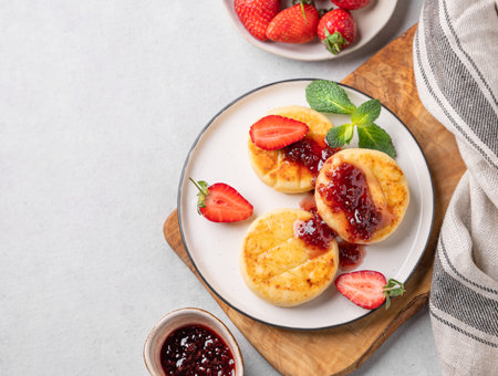 Cottage cheese, cheesecakes or syrniki sprinkled with berry sauce on a cutting board on a light background with jam, strawberry and napkin. The concept of a nutritious and healthy breakfast. Top viewの写真素材