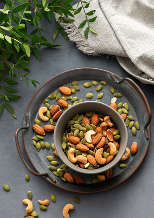 Mix of nuts. Almonds, cashews and pumpkin seeds in a bowl on a dark background with green branch. Healthy energy snack concept. Top view.の写真素材