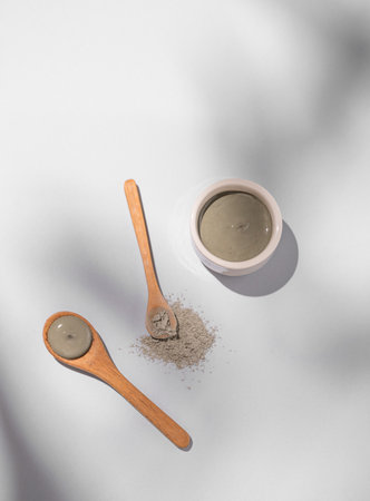 Blue clay in a bowl and spoons on a light background with shadows. Concept for preparing homemade skincare organic cosmetics and spa treatment. Top view and copy space.の写真素材