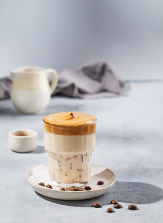 Dalgona coffee. Whipped instant coffee in a glass  with coffee beans on a blue background with shadows. The concept of a trendy and popular drink for breakfast. Free space for text.の写真素材
