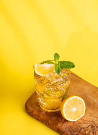A glass of iced tea with lemon and mint on a wooden board on a yellow  background with a shadow. Minimal concept of a refreshing drink or lemonade on a hot summer day. Top view.の写真素材