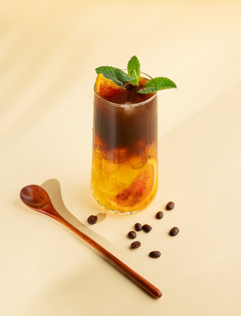 Americano coffee with orange juice (bumble) in a tall glass with ice and mint on a yellow background with coffee beans and spoon. Trendy summer Asian refreshing drink.の写真素材