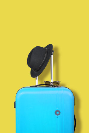 Blue suitcase and black hat on a yellow background. Travel concept. Free space for text.の写真素材