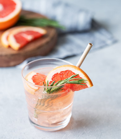 Grapefruit cocktail in a glass with rosemary and ice on a light background with fresh fruits. The concept of a trendy, summer, healthy and refreshing lemonade drink.の写真素材