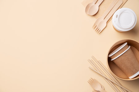 Set of eco-friendly disposable tableware with wooden cutlery, brown paper cups, bowls and bamboo straws on beige background. Concept of caring for nature with biodegradable products. Top view and copy space.の写真素材