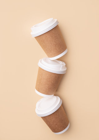 Three brown paper coffee cups with white lids on beige background. Concept of eco-friendly and careful consumption. Minimalistic mockup for product or design. Top view and copy space.の写真素材