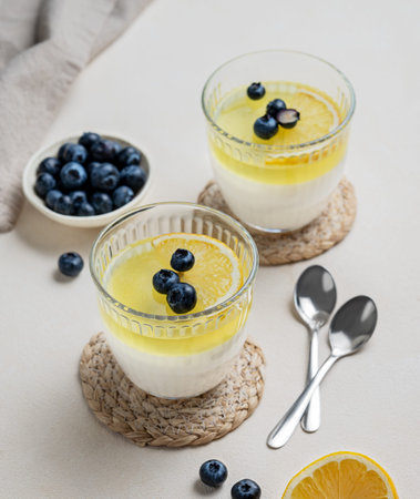 Creamy lemon panna cotta with blueberries in two glasses with fresh berries on a light background....