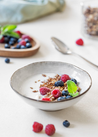 Granola with yogurt, raspberry and blueberries in a bowl on a light background close up. Concept of...