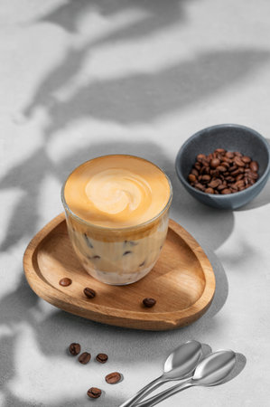 Iced dalgona coffee. Whipped instant coffee in a glass with ice on a wooden board on a gray background with coffee beans, spoon and shadow. The concept of a trendy and popular drink. Top viewの写真素材