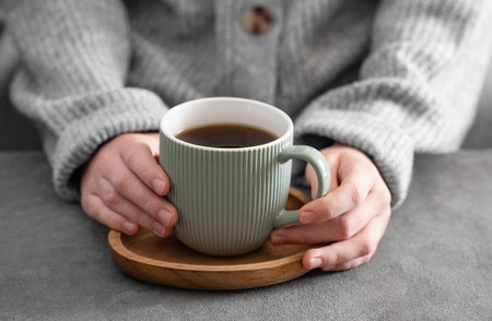 Woman in cozy sweater holding mug with espresso coffee close up on a gray table close up. Morning...