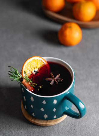 Mulled wine with orange, cinnamon and rosemary in a cup on a dark background with tangerines. The concept of a traditional winter hot drink with spices and fruits for the holiday. Top viewの写真素材