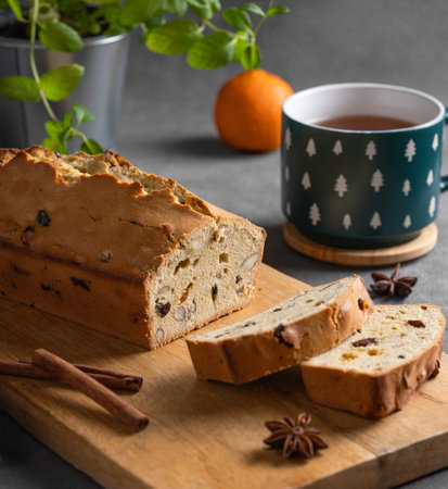 Spicy pie with fruits, nuts and spices on a wooden board, on a dark background with tangerines,...