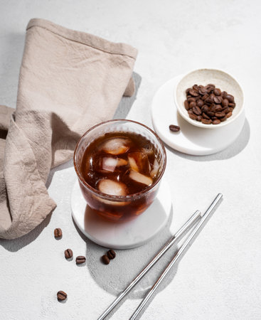 Cold brew coffee in a glass with ice on a light texture background with coffee beans, straw and shadow. Summer refreshing trendy drink. Top view.の写真素材