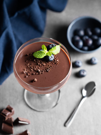 Chocolate pudding in a tall glass with mint and fresh blueberry on a dark background with chocolate pieces, berries and napkin. Homemade mousse dessert or panna cotta concept. Top  view and copy spaceの写真素材