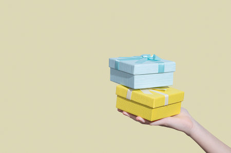 Two blue and yellow gift boxes in hand on light background. Concept of advertising layout or banner for holiday or greeting card. Free space for text.の写真素材