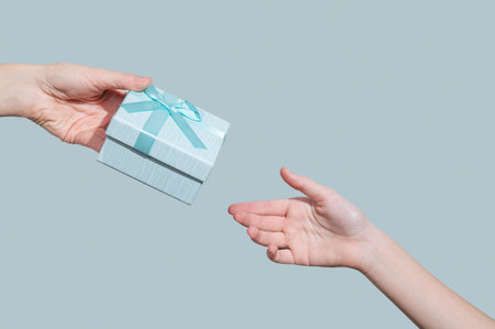 Hand with gift blue box reaching to another hand on light background. Concept of advertising layout...
