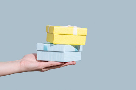 Two blue and yellow gift boxes in hand on light background. Concept of advertising layout or banner...