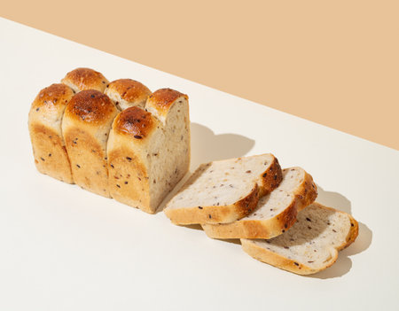Freshly baked whole grain bread with slices on beige and white background. Home baking and healthy food concept for bakery advertisement layout or menu. Top view and copy space.の写真素材