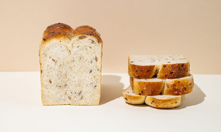Freshly baked whole grain bread with slices on beige and white background close up. Home baking and...