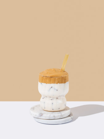 Korean whipped drink Dalgona coffee in a glass on a marble stand on a white beige background. Drink...
