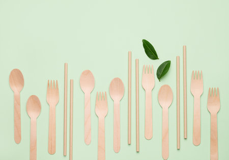 Flat lay wooden spoons, forks and straw on green background with leaves. Eco-friendly and sustainable kitchen utensils concept. Top view and copy space.の写真素材