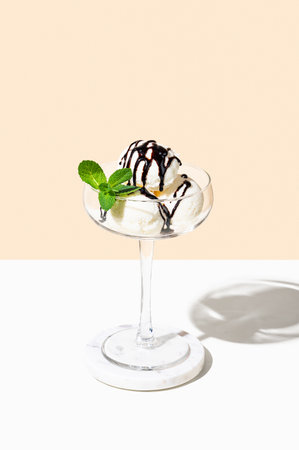 Scoops of vanilla ice cream in a tall glass with chocolate topping and a mint leaf on a light background. Summer refreshing dessert concept for a menu layout or advertising banner. Copy space.の写真素材