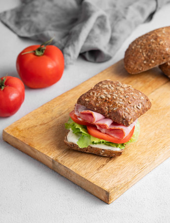 Toast sandwich made of grain bread with prosciutto, cheese, tomatoes, lettuce and sauce on a wooden board on a light background with napkin. Healthy and diet breakfast concept. Copy space.の写真素材