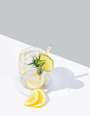 Fresh lemonade with lemon, lime, rosemary and ice. Citrus cocktail mojito on a white gray background. Summer trendy drink concept for bar menu advertising or banner. Copy space.の写真素材