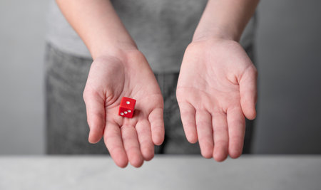 A child holds a red cube in one open palm, the other empty, against a neutral background, symbolizing decision-making or chance. The concept of gambling.の写真素材