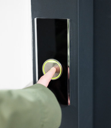 Close up of person finger pressing illuminated doorbell button on smooth black panel, minimalist real indoor environment, access concept.の写真素材