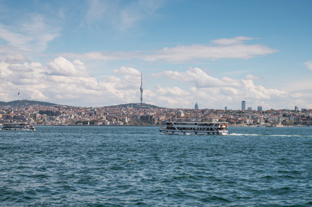White ferry sails across Bosphorus with Istanbul skyline, TV tower and cloudy blue sky in...